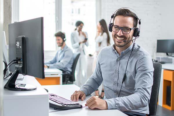 Smiling person at work with a headset on, ready to take calls and help customers.